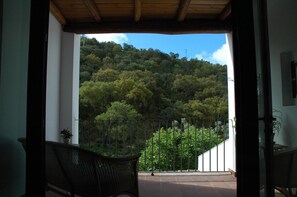 A balcony with wicker furniture, a view of a forested hillside, and a metal railing.