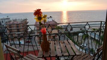 Ein Balkon mit Holztisch und Stühlen, der Blick auf die Küste mit Gebäuden und dem Meer freigibt.