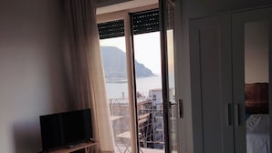 Un dormitorio con cama, televisor en un mueble, armario y balcón con vistas al mar y a la montaña.