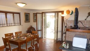 A dining area with a wooden table and chairs, a kitchen with a refrigerator and a stove, and a sliding glass door leading to an outdoor area. - Apartment in VILLA " ARIALE " (Vicopisano)