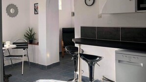 A modern kitchen with a dishwasher, a clock, and a dining area with two bar stools. - Lavender villa is set in our beautiful landscaped gardens next to the pool.  (Tsikalaria)