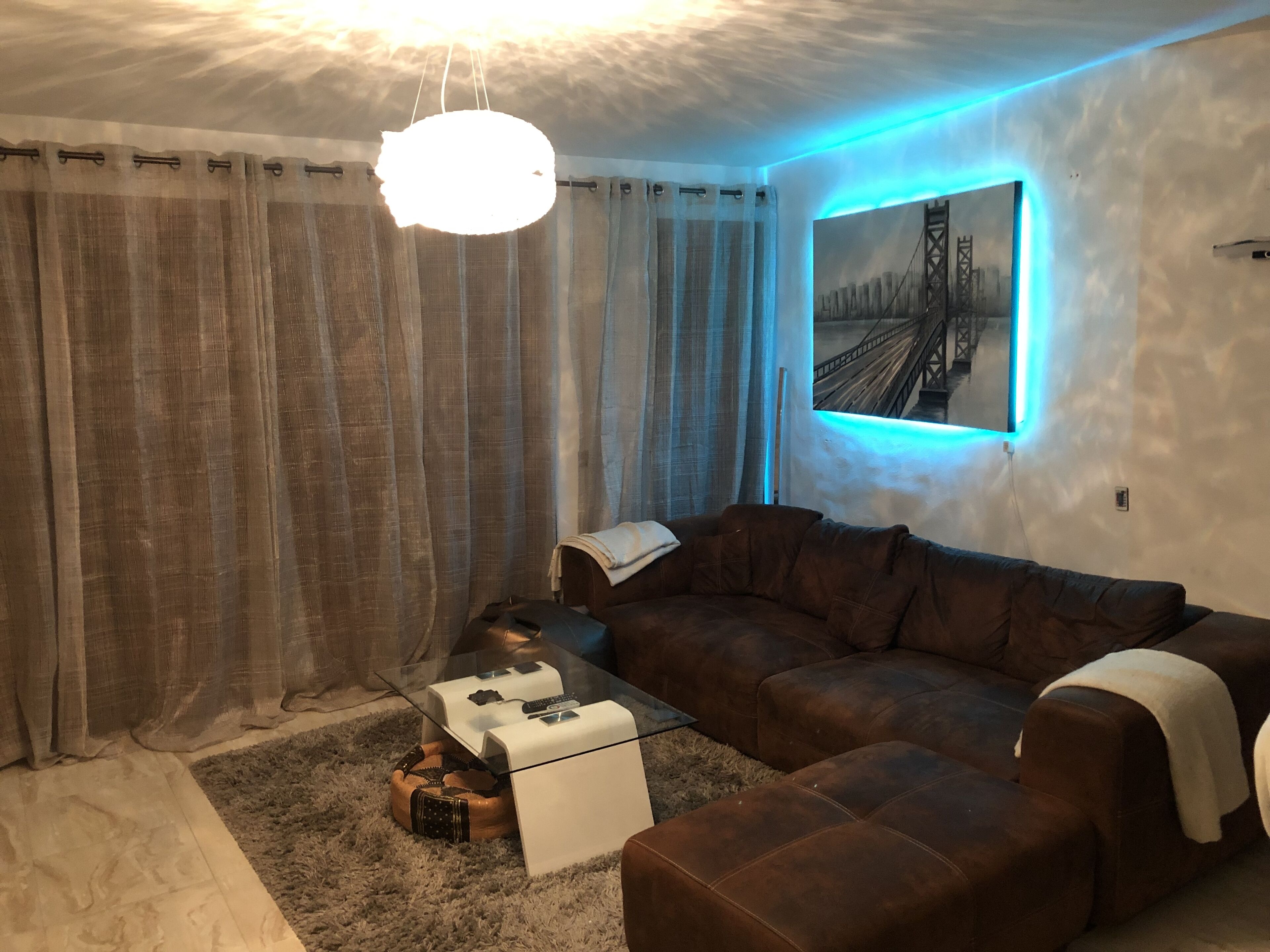 Ein modernes Wohnzimmer mit einem Ecksofa, einem Glastisch und einem Gemälde einer Brücke.
