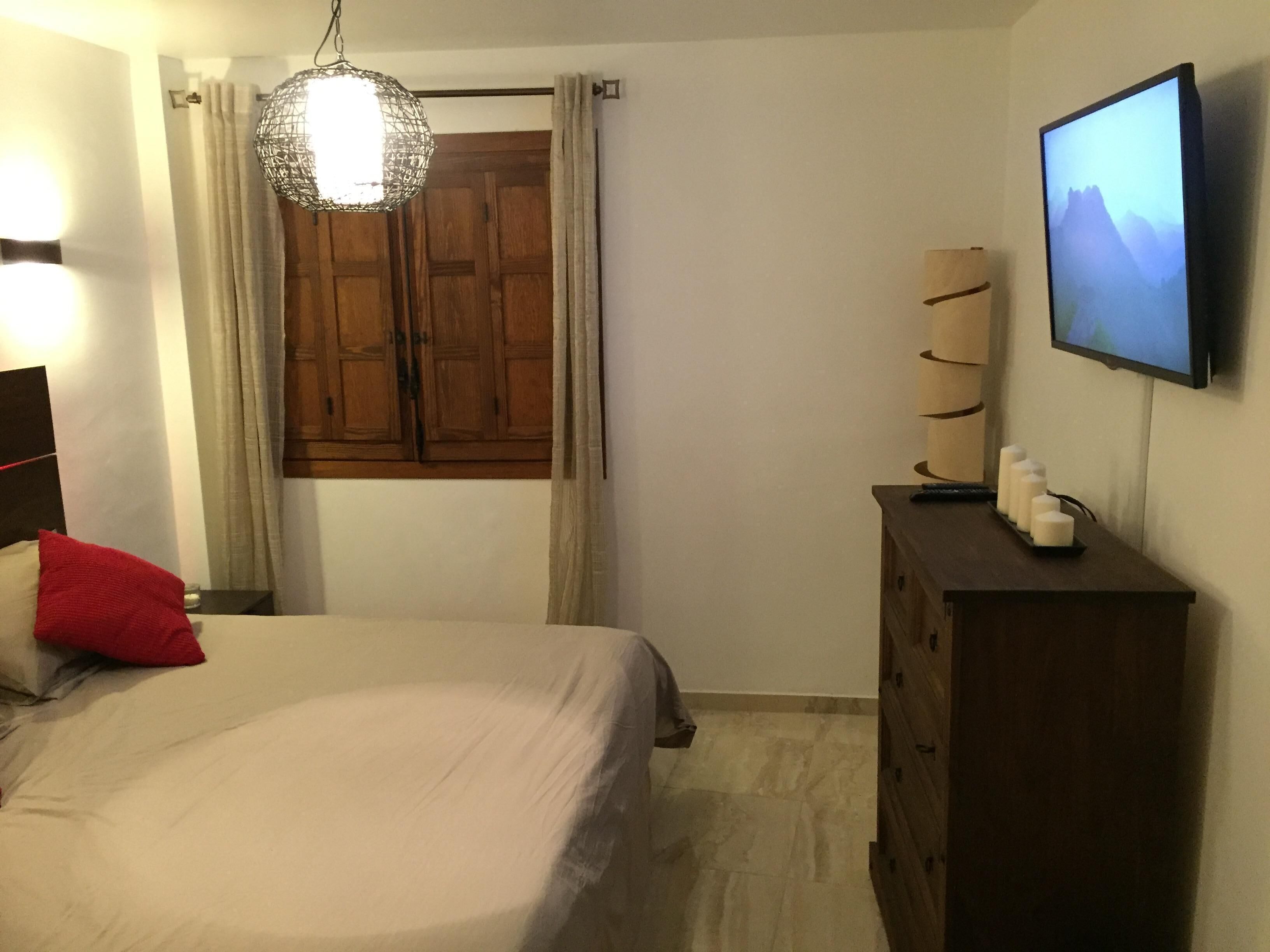 Un dormitorio con cama, cómoda, televisor y ventana con cortinas.