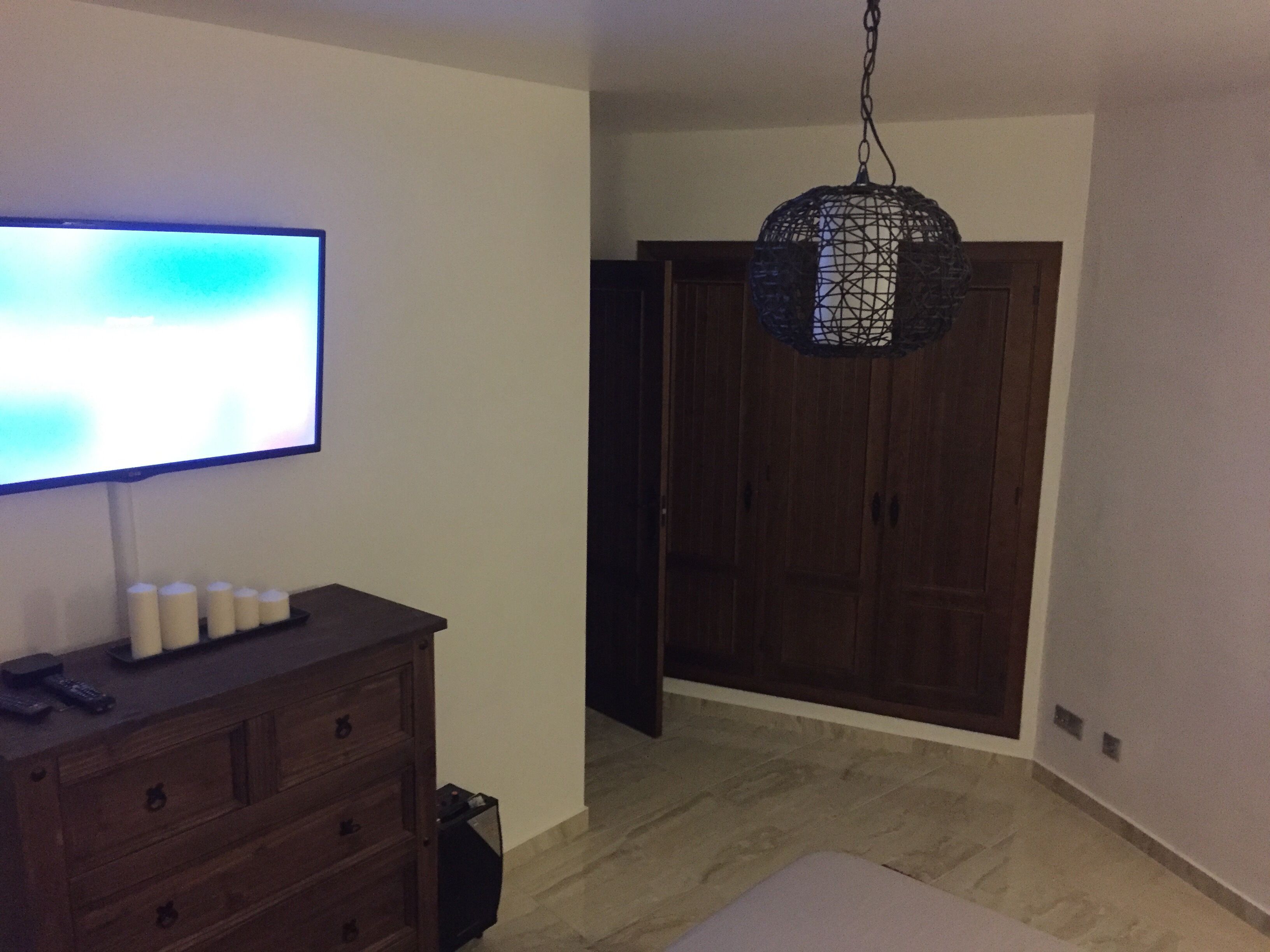 Une pièce avec un téléviseur posé sur une commode en bois, un luminaire suspendu et une armoire.