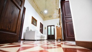 A hallway with a checkered floor, a white sofa, wooden doors, and a ceiling light.
