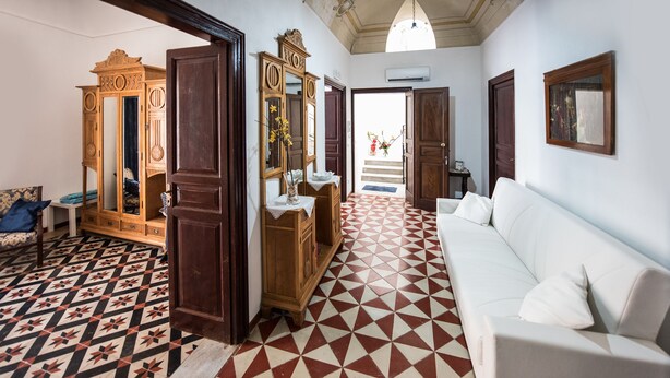 A room with a patterned floor, a white sofa, a wooden wardrobe, and a mirror.