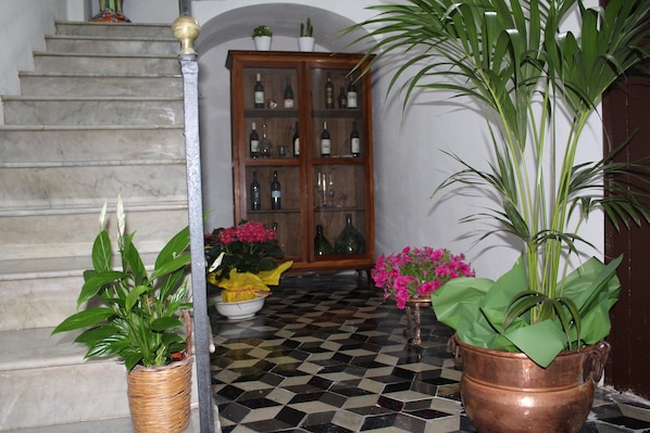 Una escalera con piso a cuadros, un aparador de madera con puertas de cristal y plantas en macetas.