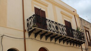 A building with a balcony, wooden doors, and a potted plant.