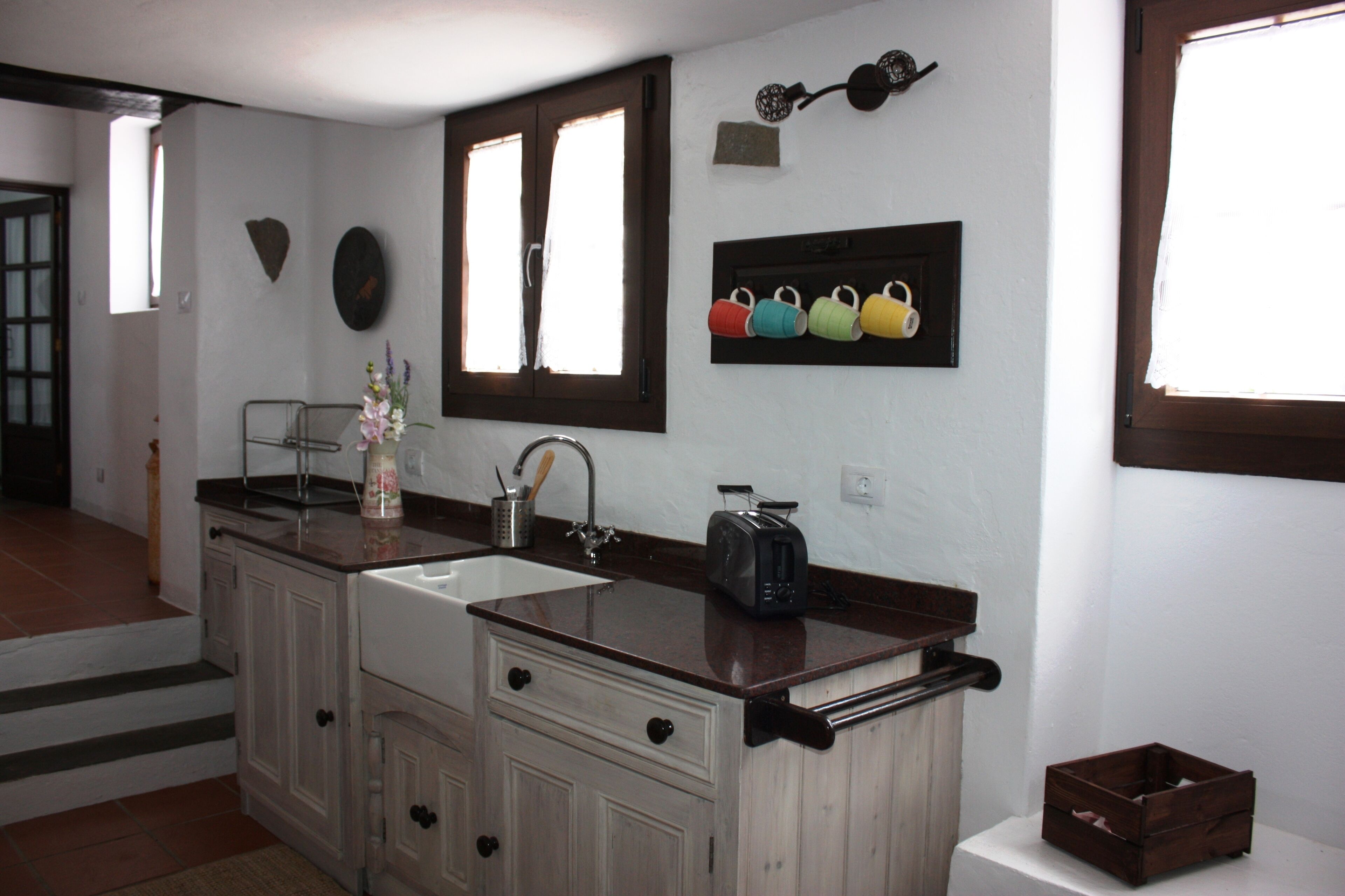 A kitchen with a double sink, a toaster, and a window with curtains.