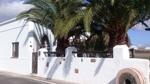 A white building with a gate, palm trees, and a clear sky. - Casa Rural La Molina large apartment in an old motor mill from 1912 (Maguez  -Lanzarote)