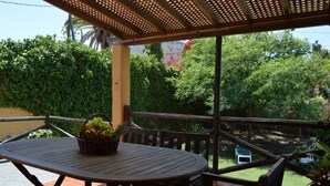 A covered patio with a round table and chairs, a basket of fruit, and a view of a lush garden. - Chalet La Alpispa with private pool in Las Palmas. (Las Palmas de Gran Canaria)