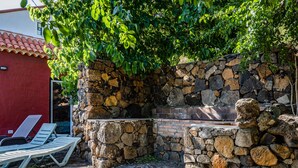 Un espace extérieur aménagé avec des sièges en pierre et un barbecue, entouré de verdure et bordé d’un bâtiment rouge.