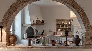 A kitchen with a brick archway, wooden shelves, and various kitchen utensils.