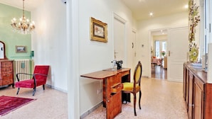 A spacious room with a wooden desk, a red chair, a vintage sewing machine, and a dining area in the background.