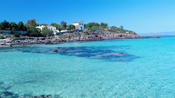 A coastal property with clear turquoise waters, rocky shoreline, and a white building with a red roof. - Comfortable and bright apartment with terrace just 300 meters from the sea (Quartu Sant'Elena)