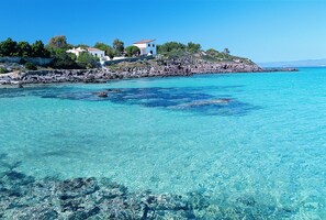 Une propriété située sur la côte, avec une eau turquoise cristalline, un rivage rocheux et un bâtiment blanc surmonté d’un toit rouge.