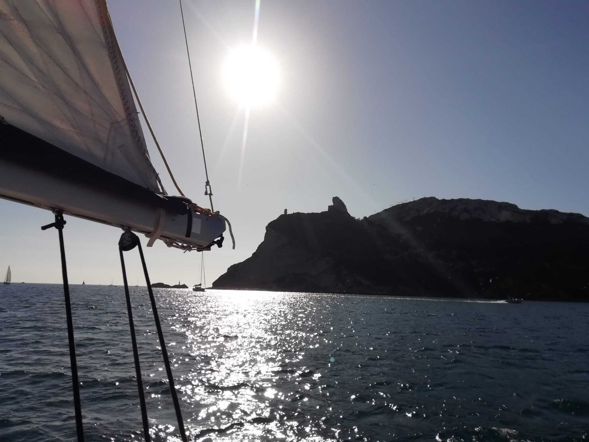 A sailboat with a clear view of the sea and a rocky coastline in the background.