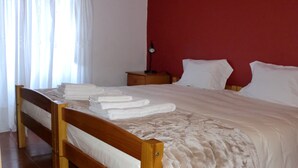 A neatly made bed with folded towels, a wooden headboard, a nightstand with a lamp, and a red wall. - Mira Porto House Cellars (Porto)