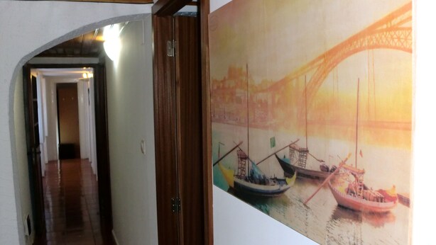 A hallway with a wooden door leading to a room with a large painting of boats on water. - Mira Porto House Cellars (Porto)