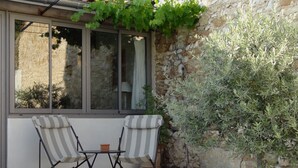 Eine Terrasse mit zwei gestreiften Stühlen, einem kleinen Tisch, einer Steinmauer und einem Baum.