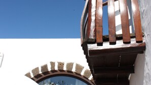 Un balcon en bois à la forme incurvée, adossé à un bâtiment à la façade blanche et doté d’une fenêtre bien visible.
