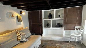 Un salon chaleureux avec un canapé, un fauteuil, une étagère ornée d’objets décoratifs et un luminaire fixé au mur.