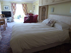 A hotel room with a large bed, a desk with a computer, a chair, a TV, and a window with curtains.