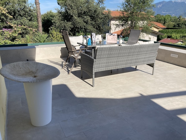 An outdoor patio with wicker furniture, a white decorative bowl, and a view of a mountainous landscape. - Italy, Tuscany, Versilia, Cinquale 400 meters from the sea and 3km from Forte dei Marmi (Capanne-Prato-Cinquale)