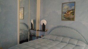 A bedroom with a bed, a bedside table, a mirror, and a painting on the wall.