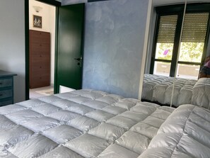 Ein Schlafzimmer mit einem großen Bett, einer grünen Tür und einem Fenster mit Jalousien.