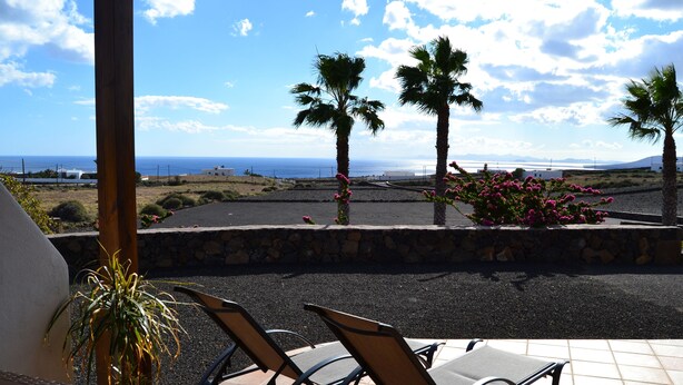 A patio with two chairs and a table, overlooking a coastal landscape with palm trees and a view of the sea. - APARTMENT LA FINCA (MÁCHER)