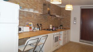A compact kitchen with a wooden countertop, white cabinets, a built-in oven, and a stainless steel sink. There are two bar stools and a hanging light fixture.