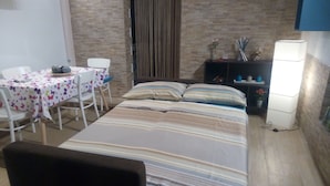 A room with a bed, a table with chairs, a small cabinet, and a lamp.
