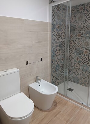 A bathroom with a toilet, bidet, and shower with patterned tiles.