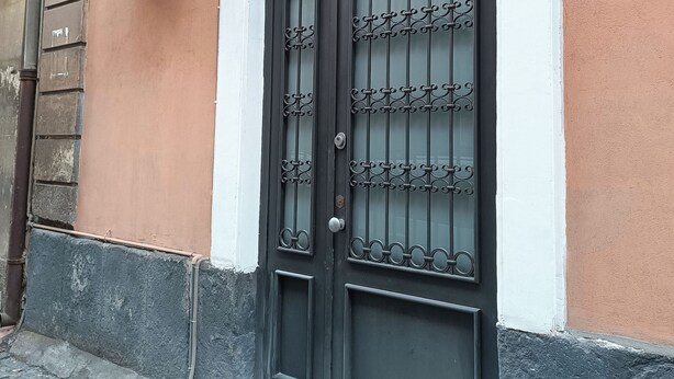A black metal gate with decorative patterns, attached to a building with a peach-colored wall and a white trim.