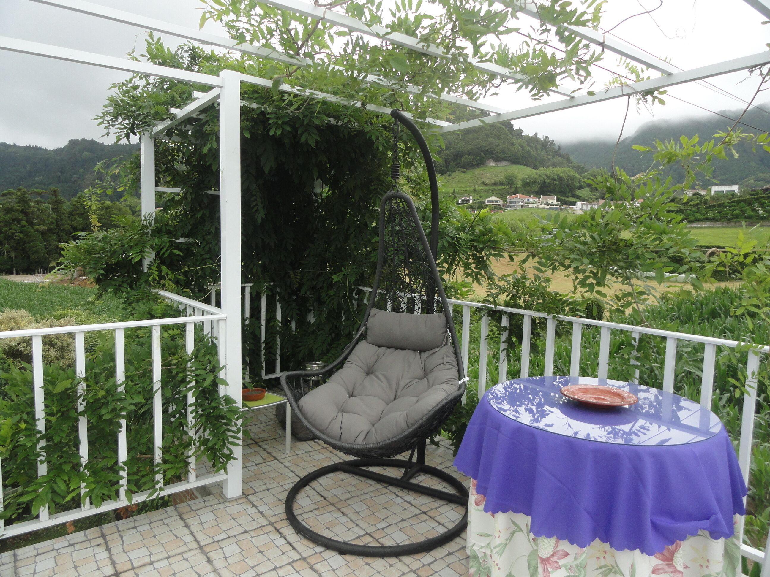 Un patio cubierto con una silla colgante y una mesa con mantel floral.