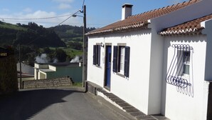 A white building with a tiled roof, a blue door, and black shutters.