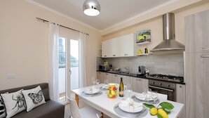 A modern kitchen with white cabinets, a stainless steel range hood, and a dining area with a white table set for four. -  LEMON IN THE AIR  (Pontone)