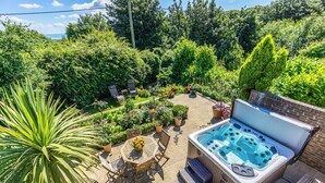 A patio area with a hot tub, surrounded by lush greenery and potted plants. - Heated indoor pool & spa, countryside holiday cottage near the beach & park (Hastings)