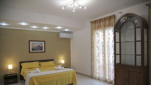 Une chambre d’hôtel comprenant un lit, des lampes de chevet, un appareil de climatisation, une grande armoire et une fenêtre avec des rideaux.