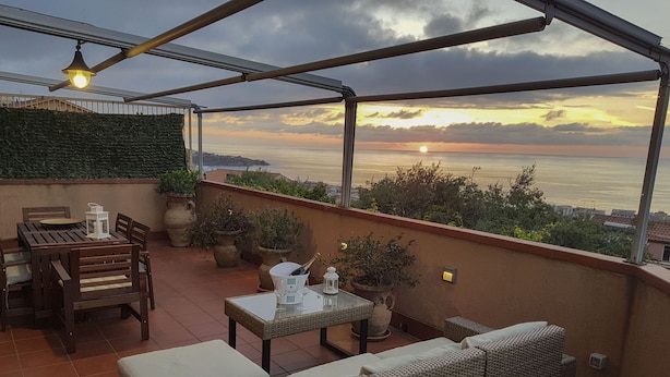 Une terrasse sur le toit offrant une vue sur le coucher de soleil sur la mer, aménagée avec une table, des chaises et un canapé.