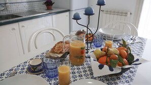 Une table de petit-déjeuner dressée avec des assiettes, des verres, un pichet de jus d’orange, du pain et un panier de fruits.