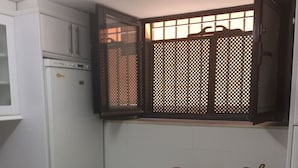 Una cocina compacta con refrigerador, microondas y alacenas. Se ve una ventana con mosquitero, y una pequeña cesta de madera sobre la encimera.