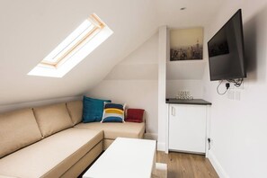 A compact living space with a sofa, a small table, a kitchenette, a TV, and a skylight. - Beautiful Loft Studio (Greater London)