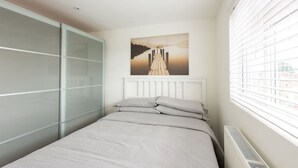 Une chambre à coucher avec un lit, une fenêtre avec des stores, un radiateur et un tableau accroché au mur.