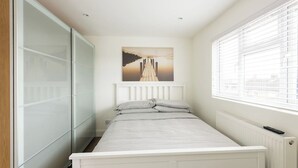 Une chambre à coucher avec un lit, un radiateur, une fenêtre avec des stores et un tableau accroché au mur.