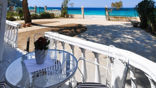 Un patio con una mesa y sillas de vidrio, baranda blanca y vista a la playa y al mar.