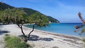 Una playa con mar azul cristalino, una orilla arenosa y una colina con vegetación escasa.