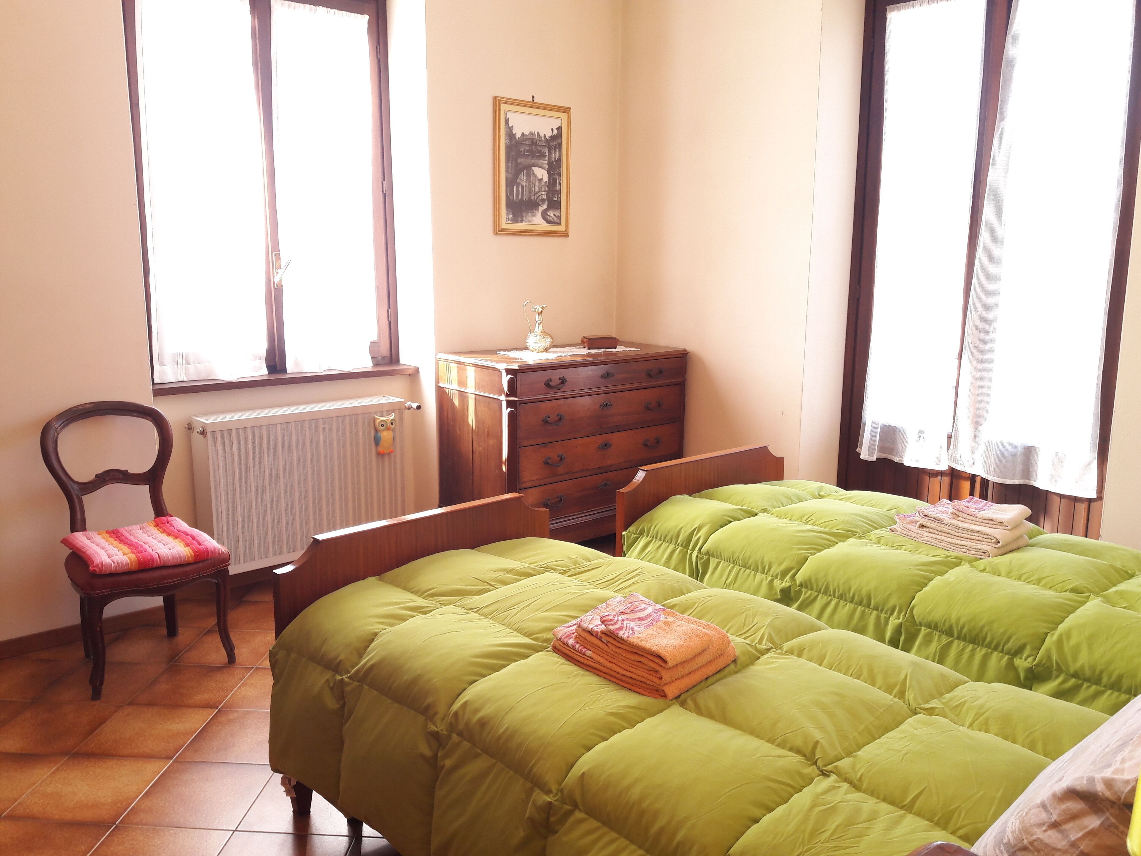 Een slaapkamer met twee bedden, een houten dressoir, een stoel en een radiator.