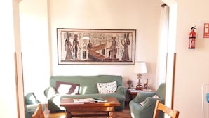 Un comedor con una mesa preparada para cuatro, un sofá verde, un cuadro en la pared y un extintor.